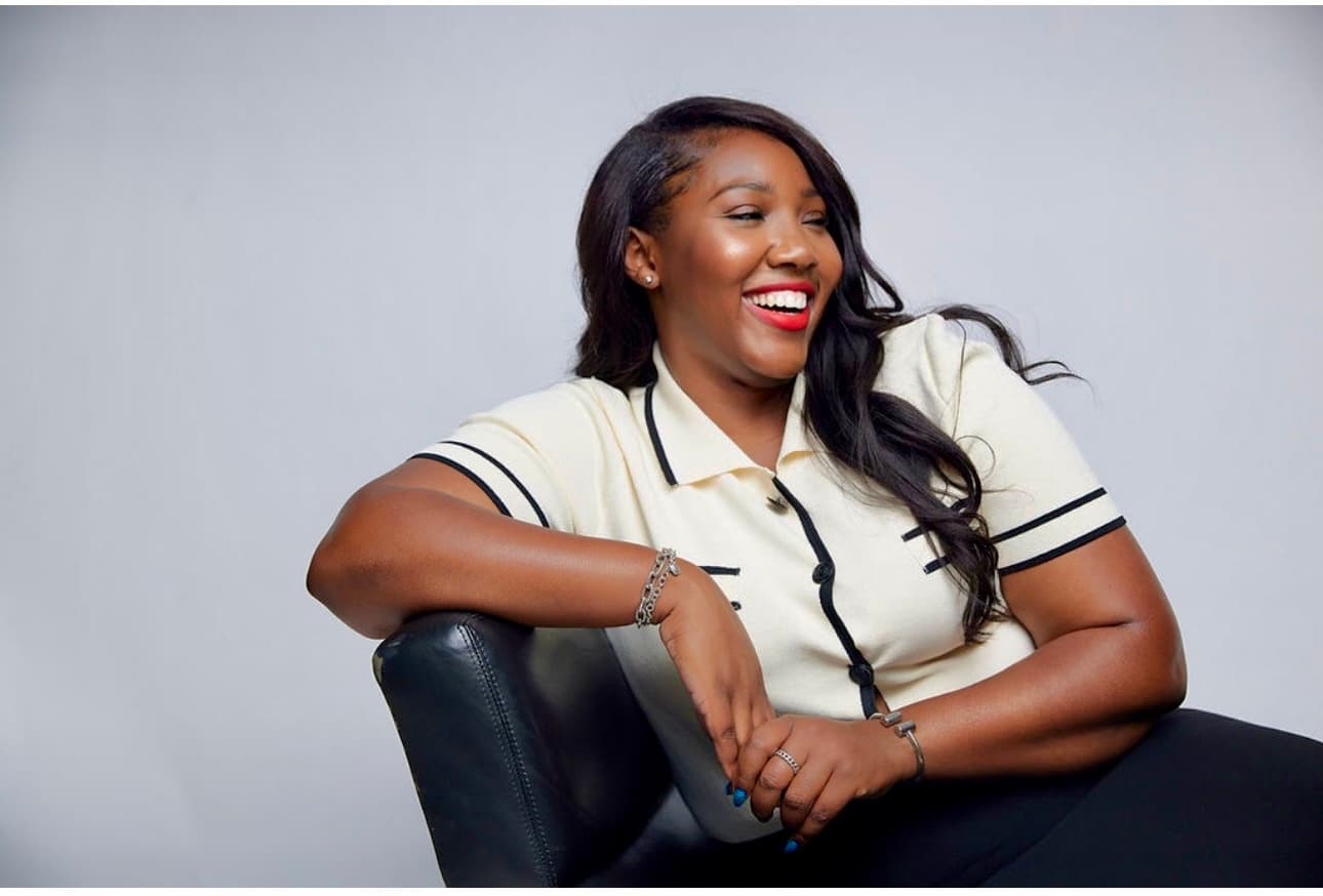 Maya J. Hicks, founder of SUKEY, laughing and leaning on the arm of a black leather chair